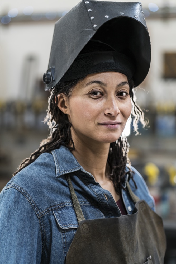 Metal Workshop,USA,Portrait of woman wearing apron and welding mask standing in metal workshop, smiling at camera.