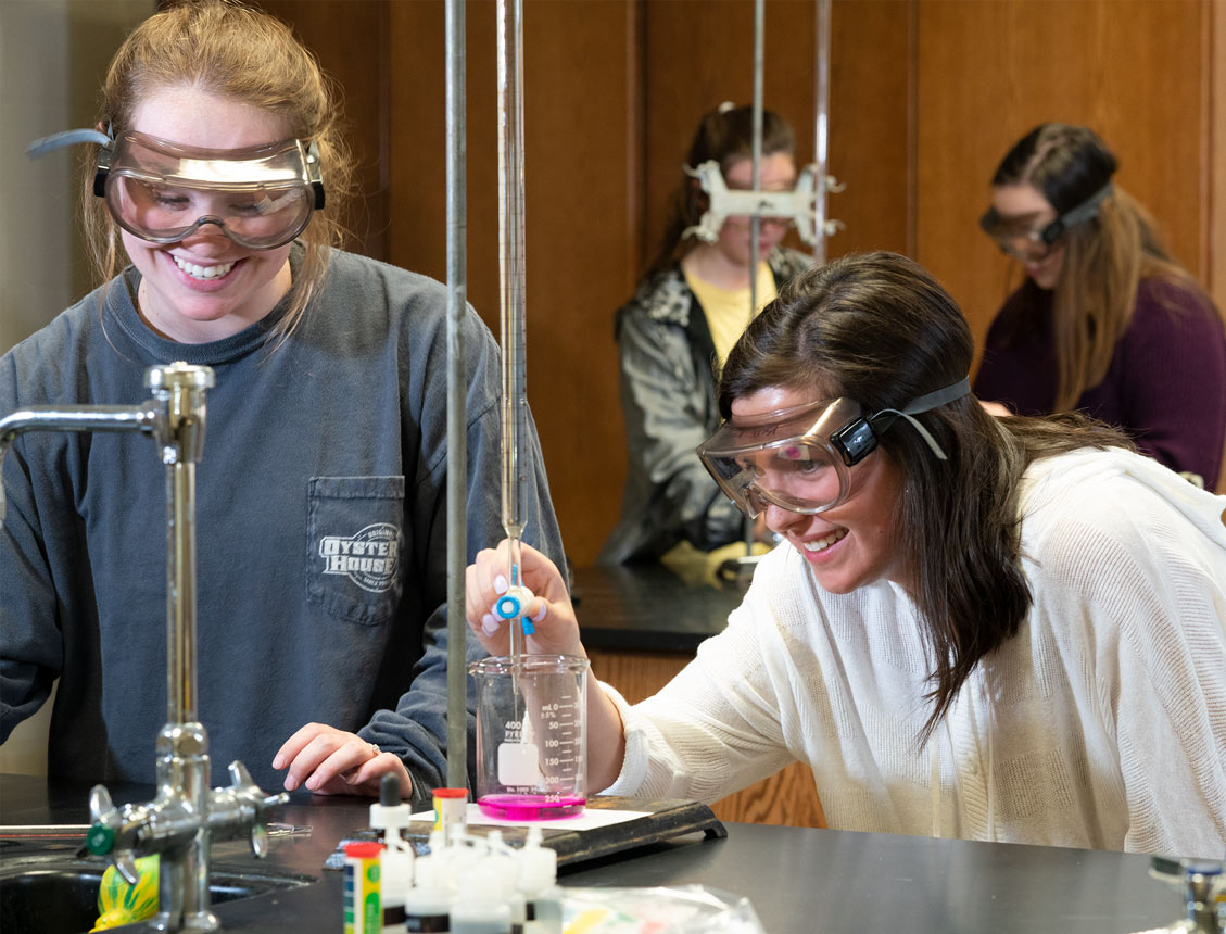 Girls in lab with goggles on smiling while doing an experiment
