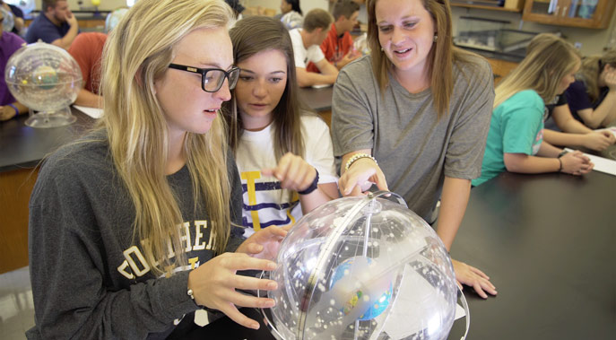 Three female students observing a globe