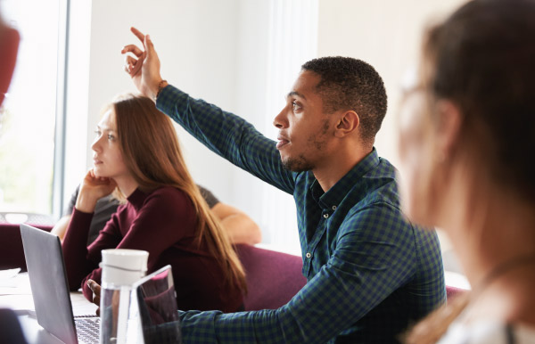 Male raising his hand to ask a question in a classroom on his laptop